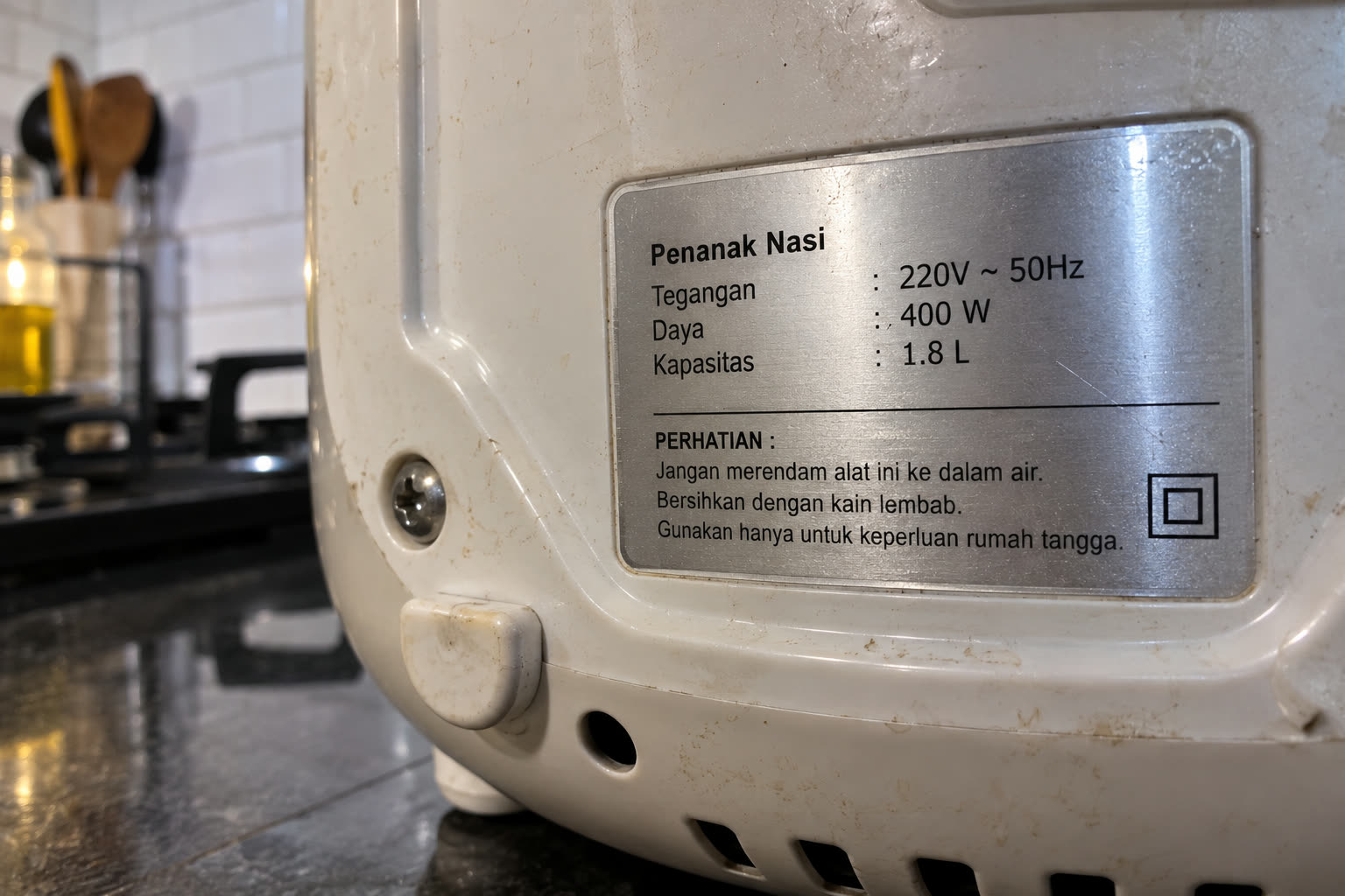 Pelat spesifikasi di bagian belakang rice cooker: tegangan 220V, daya 400 W, kapasitas 1,8 liter. Angka daya inilah yang dijumlahkan.