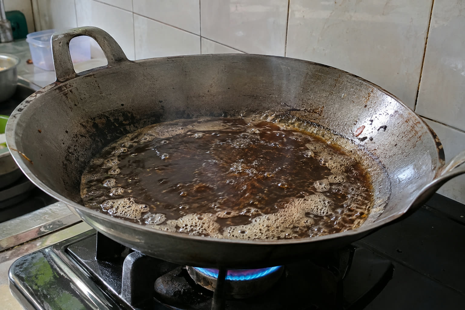 Minyak bekas yang dipanaskan di wajan: warnanya gelap, dan busa menetap di permukaan padahal belum ada bahan yang dimasukkan. Minyak seperti ini sudah waktunya dibuang.